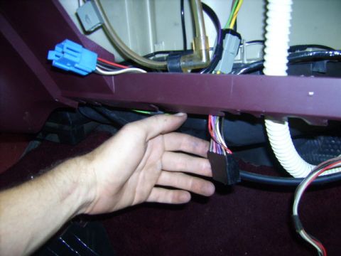 1982 Ford LTD Crown Victoria - Under-dash wiring work in a car with maroon interior: a hand holds a multi-pin black connector on a striped harness beneath the dash lip, w…