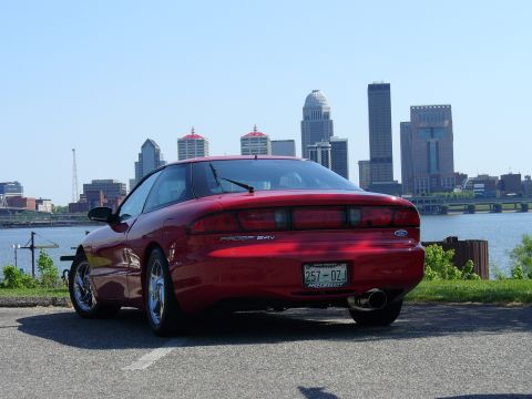 1991 Ford Probe - A red 1991 Ford Probe 24v is parked near a waterfront with the Louisville skyline visible.