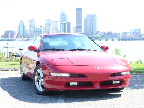 1991 Ford Probe - A red 1991 Ford Probe is parked with a city skyline in the background.