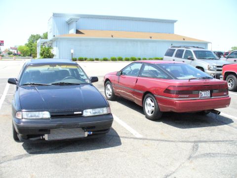 1991 Ford Probe - Two cars, a red 1991 Ford Probe and a black Mazda, are parked in a lot.