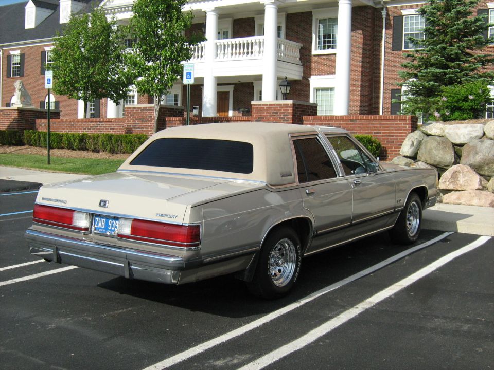 Rear three-quarter of a tan Mercury sedan in front of brick building