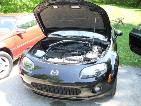 1991 Ford Probe - The front view of a black Mazda MX-5 Miata shows its engine compartment with the hood raised, parked outdoors.