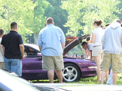 1991 Ford Probe - A group of people gather around a purple 1991 Ford Probe GT with its hood open, parked outdoors on a sunny day.