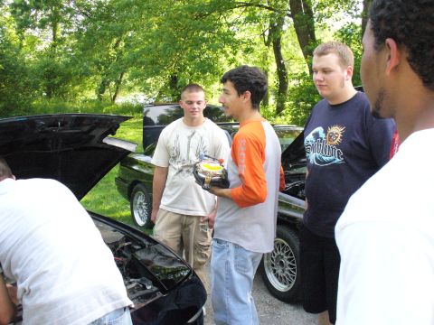 1991 Ford Probe - Men inspect car engines outdoors, with one person holding a car part for examination.
