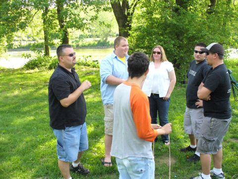 1991 Ford Probe - Several people stand in a grassy area with trees and a river in the background.