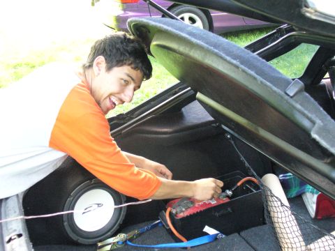 1991 Ford Probe - Person working on car battery and subwoofer in trunk, with another vehicle in background.