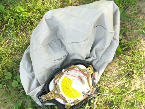 1991 Ford Probe - A deployed airbag module, showing its internal components and part number, rests on a grassy surface.