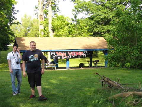 1991 Ford Probe - A gathering appears to be taking place under a picnic shelter adorned with 'MDY MAZDAS' graffiti and multiple Mazda logos.