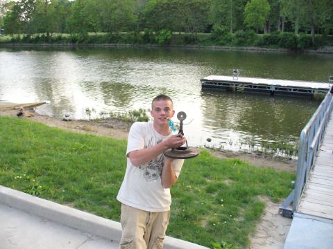 1991 Ford Probe - A man stands by a lake holding a sculpture crafted from automotive parts.