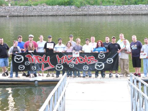 1991 Ford Probe - A group of people gathered on a dock, holding a large banner with the text "IMDY MAZDAS" and multiple Mazda logos.