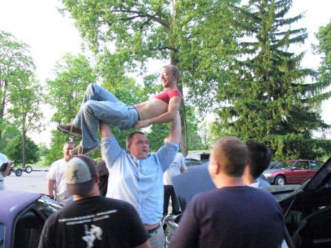 1991 Ford Probe - A group of people are gathered around cars, with one man lifting another man overhead.