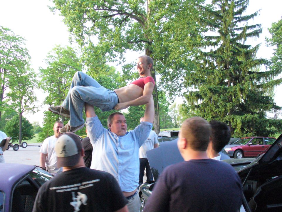 guy lifting another guy over his head, people watching, cars around