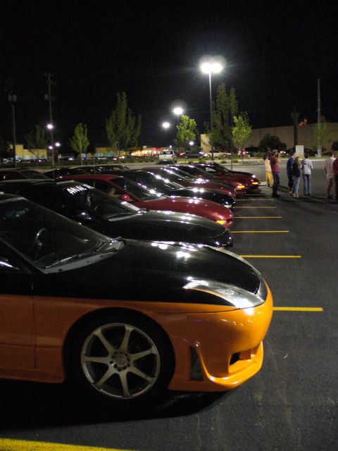 1991 Ford Probe - A line of cars are parked in a lot at night under streetlights.