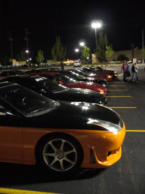 1991 Ford Probe - Several cars are parked in a lot at night under streetlights, with a two-tone orange and black car in the foreground.
