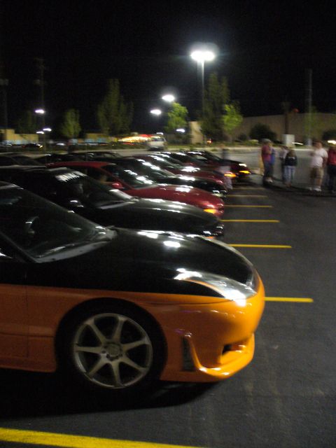 1991 Ford Probe - A line of cars are parked in a lot at night, illuminated by streetlights.