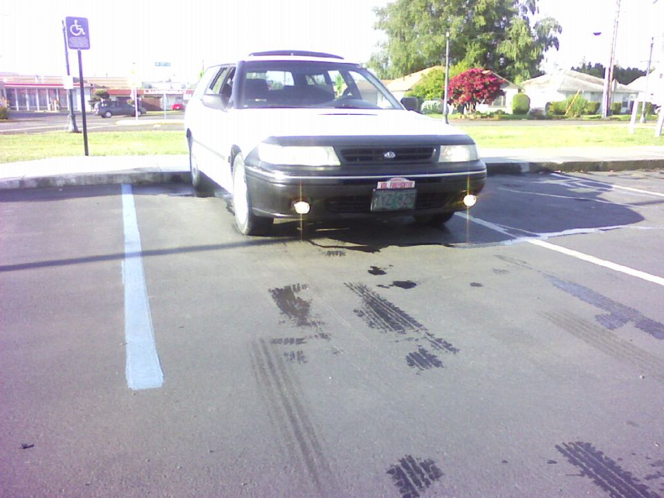 White station wagon with black front end parked, viewed from front with skid marks on pavement