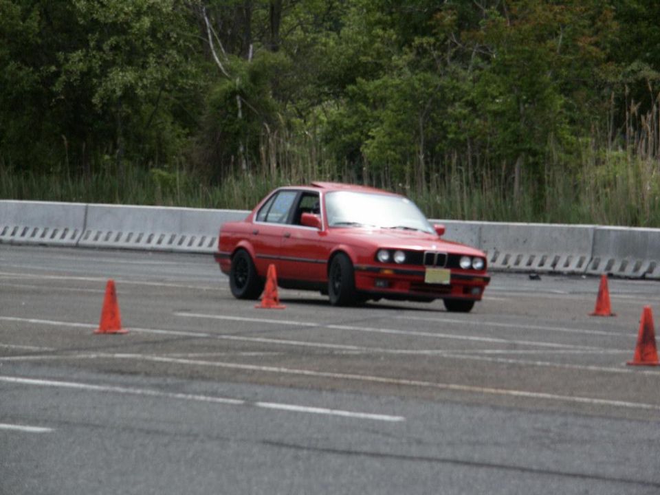 Red sedan with sunroof and black wheels on a track, front 3/4 view
