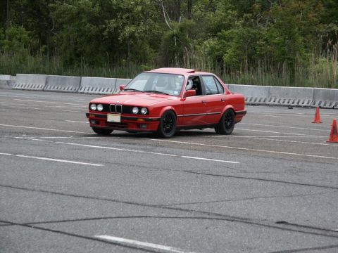 2001 Mercury Grand Marquis - Red sedan with black wheels on a track, driver visible inside. Orange cones are on the side.