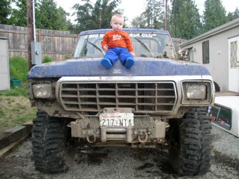 1979 Ford Bronco - A child sits on the muddy hood of a blue 1979 Ford Bronco, which is heavily modified for off-road use.