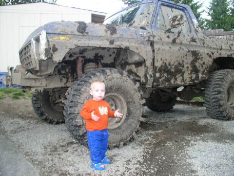 1979 Ford Bronco - A small child poses next to a heavily mud-caked off-road vehicle, highlighting its massive tires.