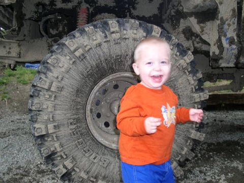1979 Ford Bronco - A smiling child stands next to a massive, mud-caked off-road tire, highlighting the scale of the vehicle's components.