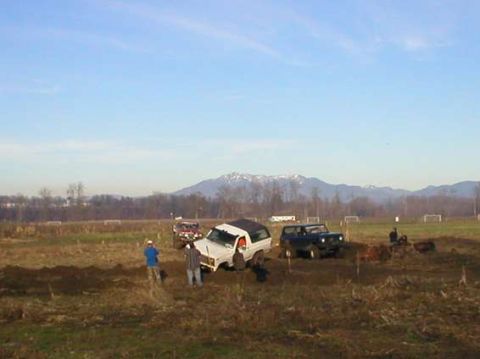 1979 Ford Bronco - Several off-road vehicles, including a 1979 Ford Bronco, are stuck in a muddy field with mountains in the background.