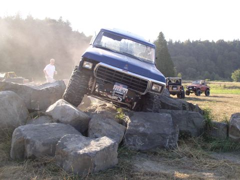 1979 Ford Bronco - A blue off-road SUV navigates a rocky obstacle course with other vehicles in the background.
