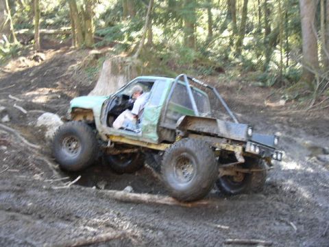 1979 Ford Bronco - Off-road pickup truck navigates a steep, muddy incline in a wooded area.
