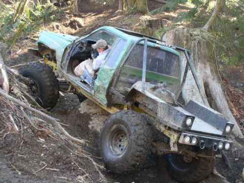 1979 Ford Bronco - A heavily modified truck navigates a steep, muddy incline in a wooded area.