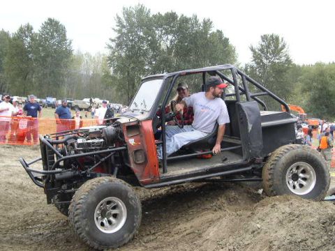 1979 Ford Bronco - A custom-built off-road buggy with a roll cage and exposed engine is seen on a dirt track with spectators in the background.
