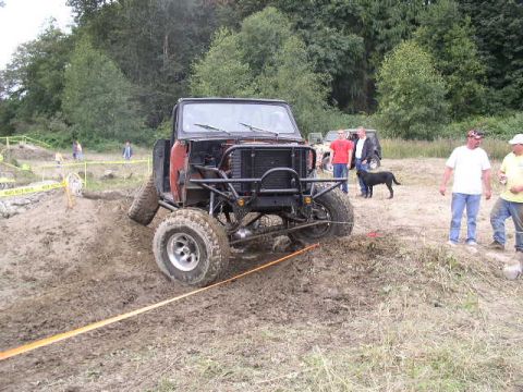 1979 Ford Bronco - This modified 1979 Ford Bronco is navigating a muddy off-road course. Multiple people and other vehicles are visible.