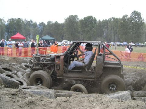 1979 Ford Bronco - Off-road vehicle navigates a muddy obstacle course with spectators in the background.