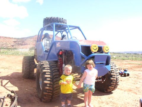 1979 Ford Bronco - A custom off-road buggy with oversized tires and smiley face headlights is shown with two children posing in front of it.