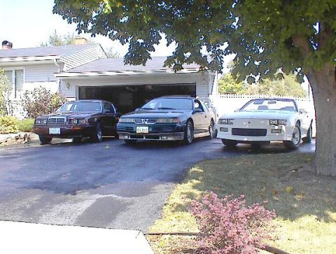2004 Ford Mustang - Three cars are parked in a residential driveway. The white car on the right is a convertible.