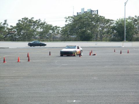 2001 Mercury Grand Marquis - A sports car maneuvers through a cone course on a paved lot, with another car visible in the background.