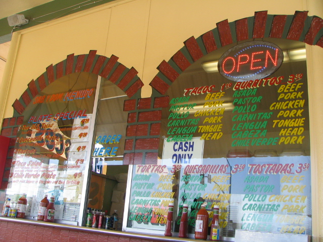 Restaurant window with menus for tacos, burritos, tortas, quesadillas, and tostadas. An "OPEN" sign is illuminated