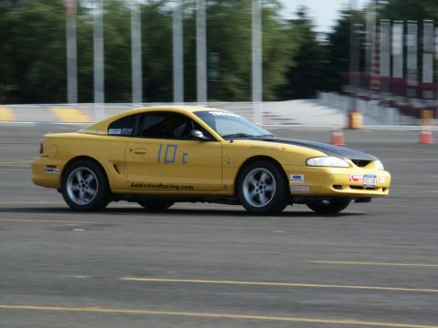 2001 Mercury Grand Marquis - A yellow coupe with a black hood is seen on a race track, displaying racing decals and the number 10c.