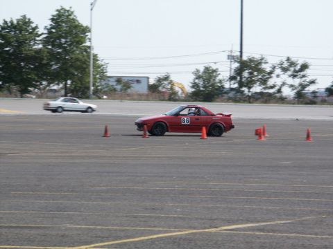 2001 Mercury Grand Marquis - A red sports car navigates a course marked by traffic cones, with another car visible in the background.