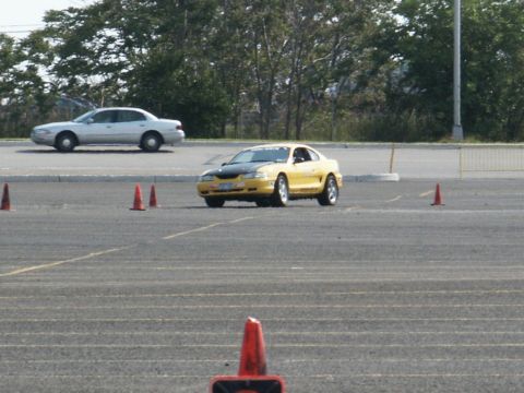 2001 Mercury Grand Marquis - A yellow coupe navigates a course marked by orange cones, with another sedan in the background.