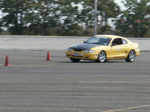 2001 Mercury Grand Marquis - Yellow 1994 Ford Mustang coupe with black hood navigates a course marked by orange cones.