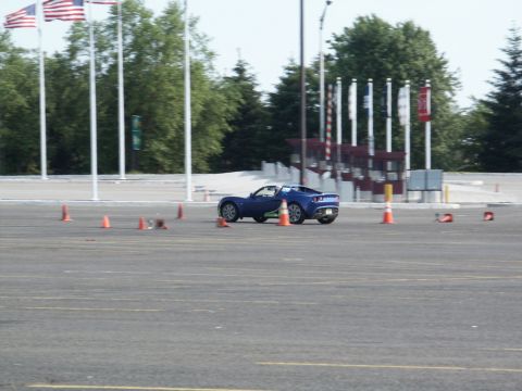2001 Mercury Grand Marquis - A blue sports car is seen on a track with cones, with American flags in the background.