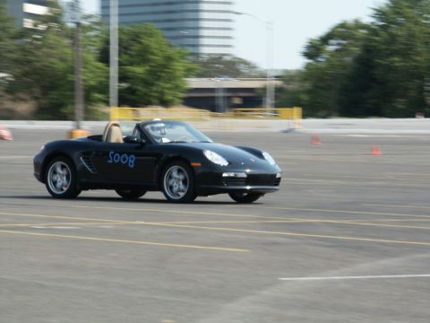 2001 Mercury Grand Marquis - A black convertible Porsche Boxster is shown in motion on a paved surface, with orange cones visible in the background.