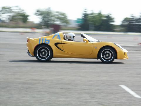 2001 Mercury Grand Marquis - A yellow sports car with blue racing numbers is seen on a track, with a driver wearing a helmet.