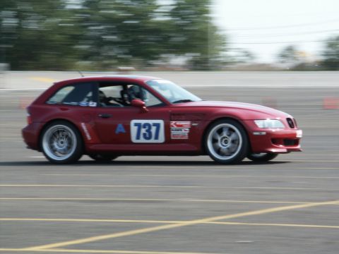 2001 Mercury Grand Marquis - A red BMW coupe with racing decals is captured in motion on a paved track.