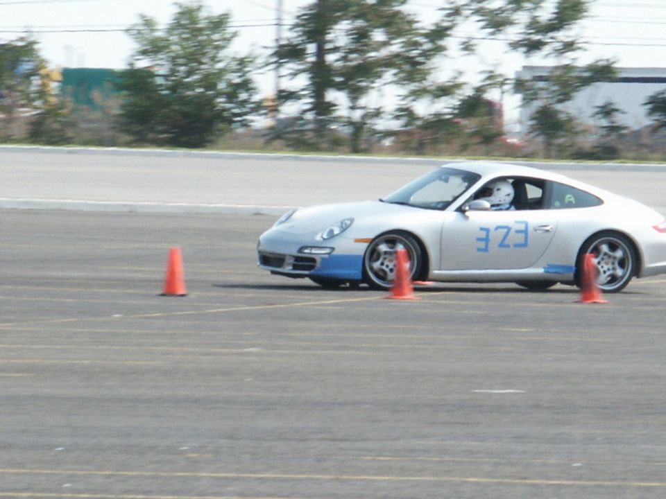 Silver Porsche 911 with blue racing stripes and the number 323 on the door, on a race track with orange cones