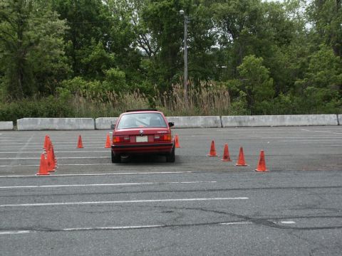 2001 Mercury Grand Marquis - A red BMW E30 sedan is seen from the rear, maneuvering through an obstacle course set up with traffic cones.