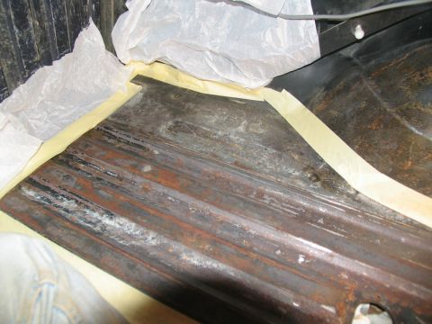 1978 Ford Bronco - A section of a vehicle's floor, showing rust and masking tape, likely prepared for repair or painting.