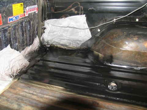 1978 Ford Bronco - The interior of a truck bed shows fresh black coating, with protective paper covering some areas.