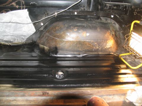 1978 Ford Bronco - The interior floor pan of a vehicle shows signs of rust and has a covered wheel well, lit by a work light.