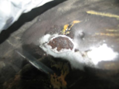 1978 Ford Bronco - A close-up view shows a patch of rust on a dark surface, surrounded by white material and some yellow discoloration.